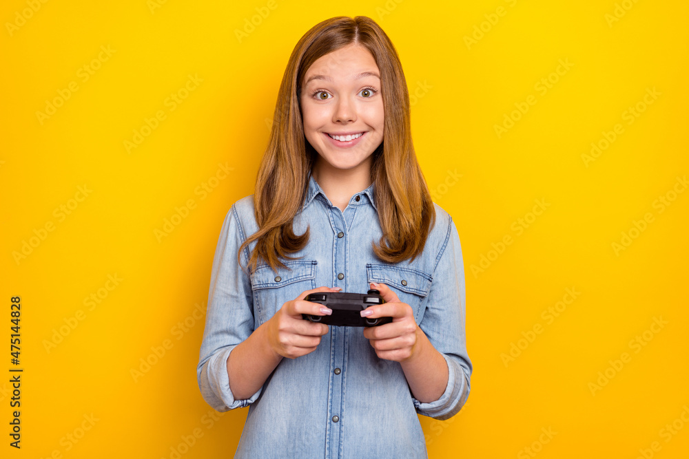 Photo of impressed teen brown hairdo girl playstation wear denim shirt isolated on bright yellow color background Photo of impressed teen brown hairdo girl playstation wear denim shirt isolated on bright yellow color background