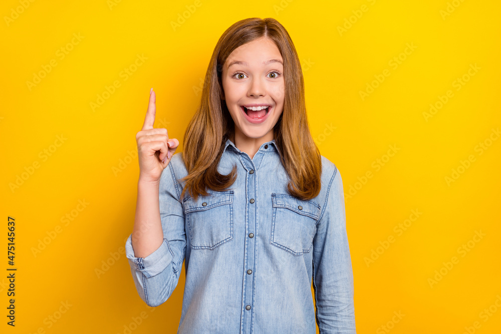 Photo of cool teen blond girl index up wear jeans cloth isolated on vivid yellow color background Photo of cool teen blond girl index up wear jeans cloth isolated on vivid yellow color background