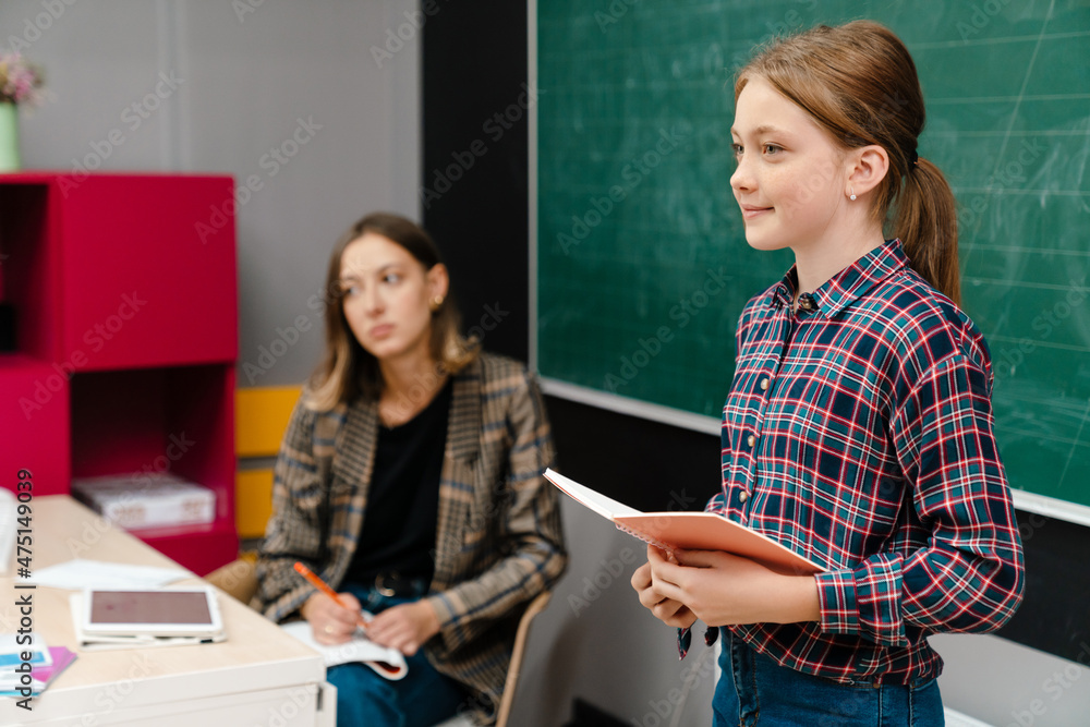 Ginger girl reading book while standing by blackboard during class Ginger girl reading book while standing by blackboard during class