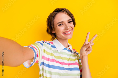 Photo of cool young brunette lady do selfie show v-sign wear white t-shirt isolated on yellow color background