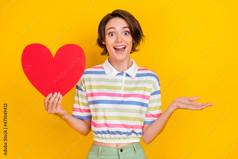 Photo of impressed young brunette lady hold heart wear white t-shirt isolated on yellow color background Photo of impressed young brunette lady hold heart wear white t-shirt isolated on yellow color background