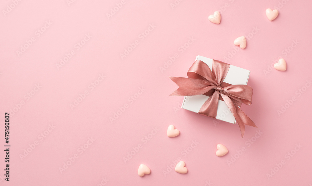 Top view photo of valentine's day decorations white giftbox with pink silk ribbon bow and small hearts on isolated pastel pink background with copyspace Top view photo of valentine's day decorations white giftbox with pink silk ribbon bow and small hearts on isolated pastel pink background with copyspace
