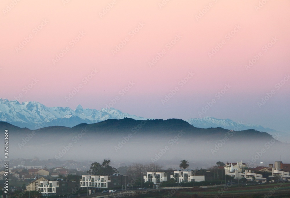 Dawn view of snow capped Picos de Europa mountain range with low lying foreground fog Santander Cantabria Spain December 2021