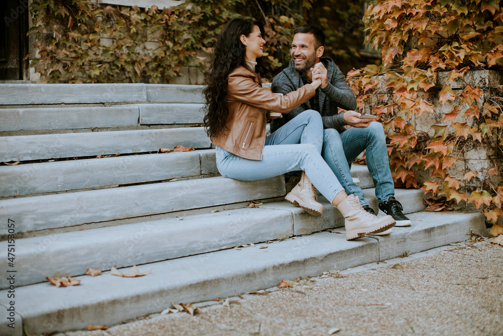 Young couple sitting on outdoor stairs on a autumn day and using mobile phone