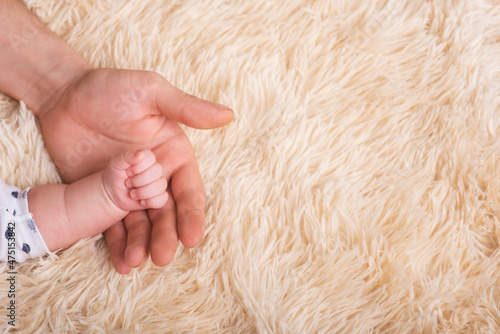 Dad holds in his hands a small baby hand. Small hand of a newborn baby in large hands of dad. Baby holds father's finger