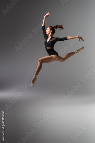pretty ballerina in pointe shoes and black bodysuit jumping on dark grey