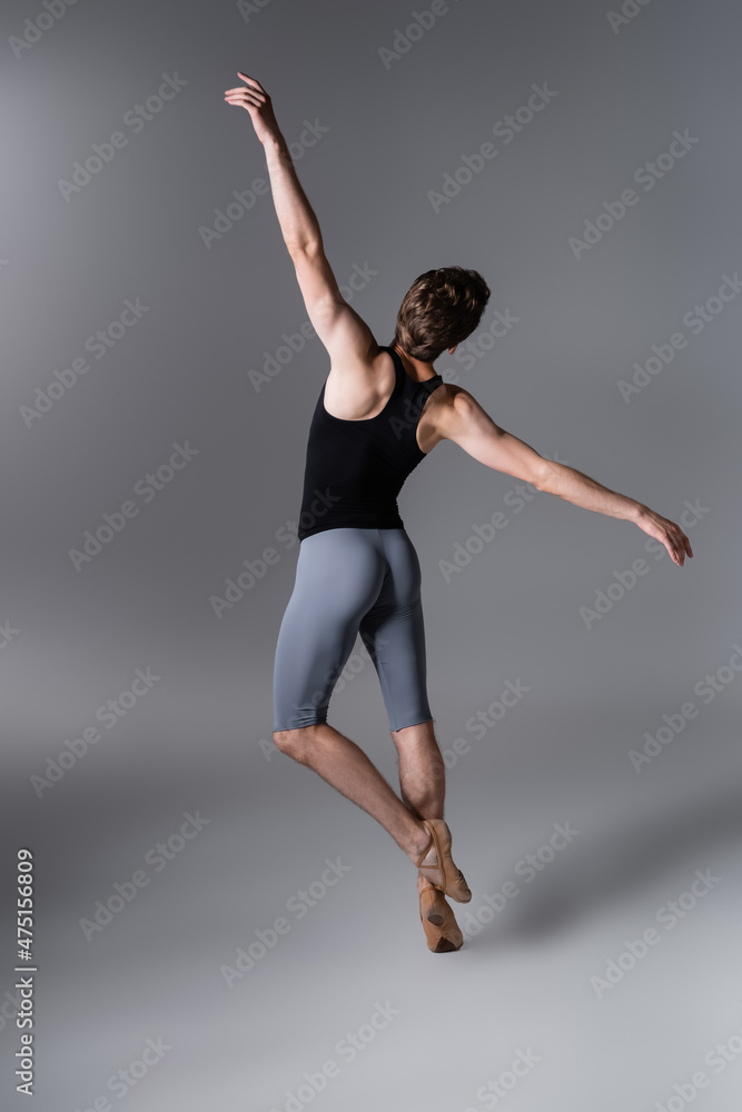 Obraz premium back view of young man in ballet shoes performing ballet dance on dark grey