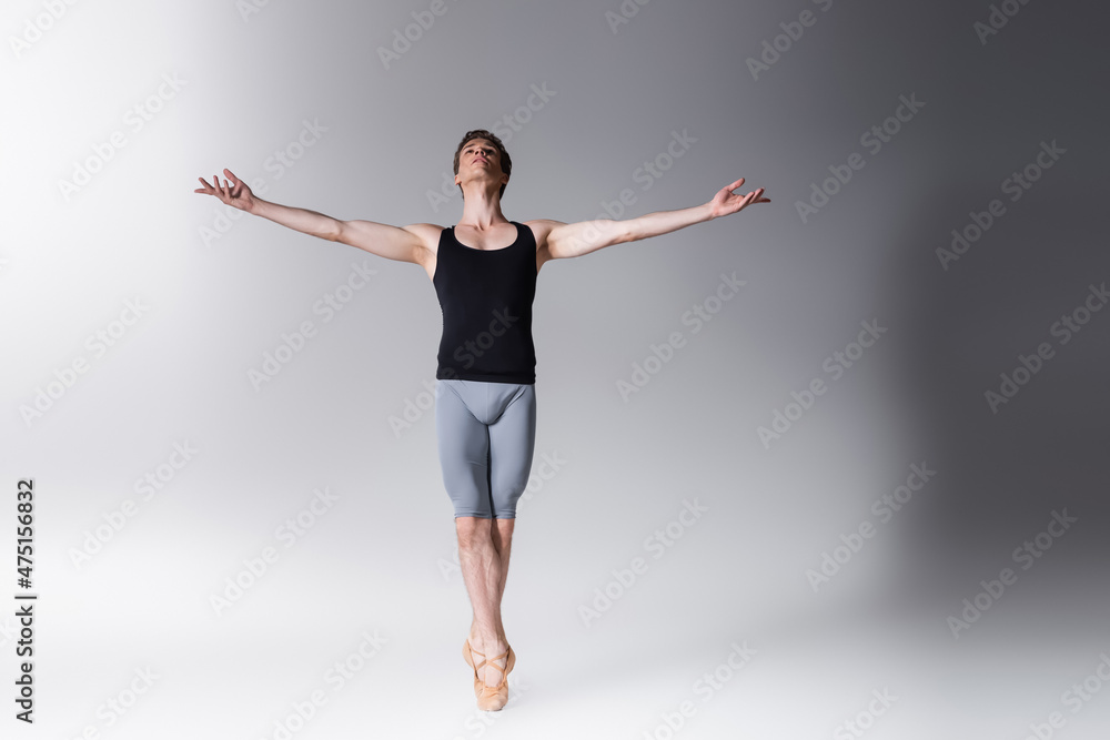 full length of young ballet dancer performing dance with outstretched hands on dark grey