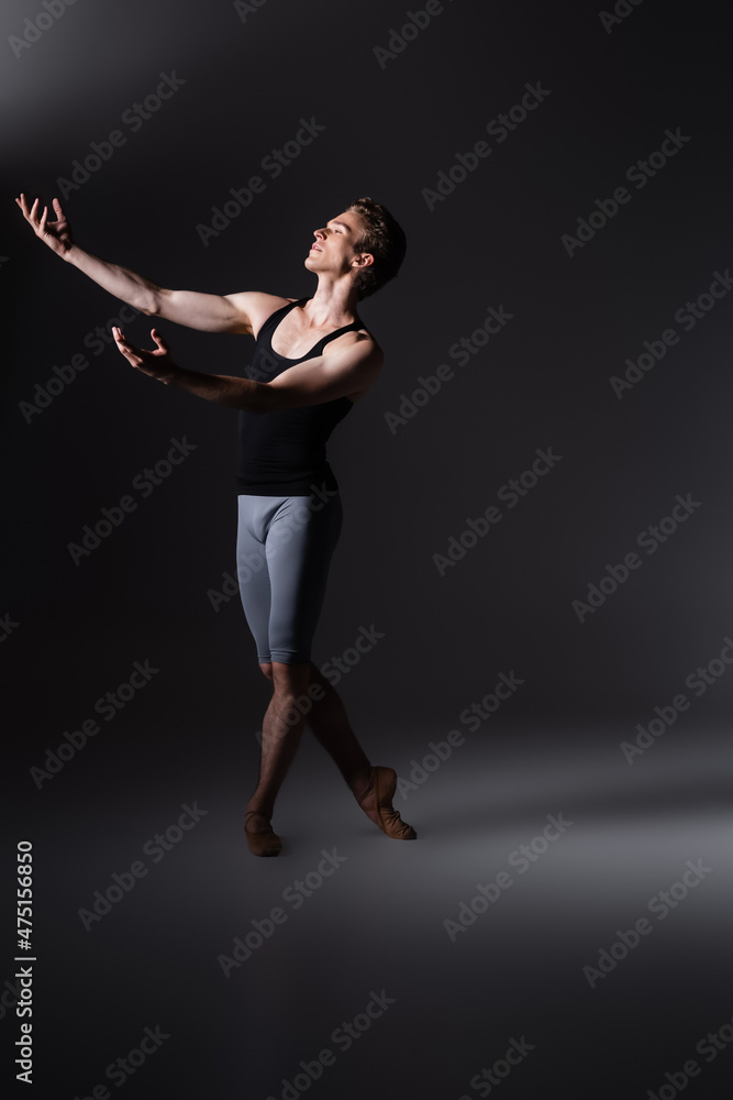 graceful dancer with outstretched hands performing ballet dance on black