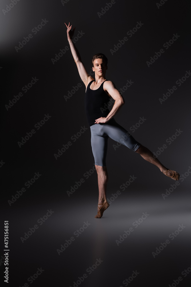 graceful man with outstretched hand performing ballet dance on black