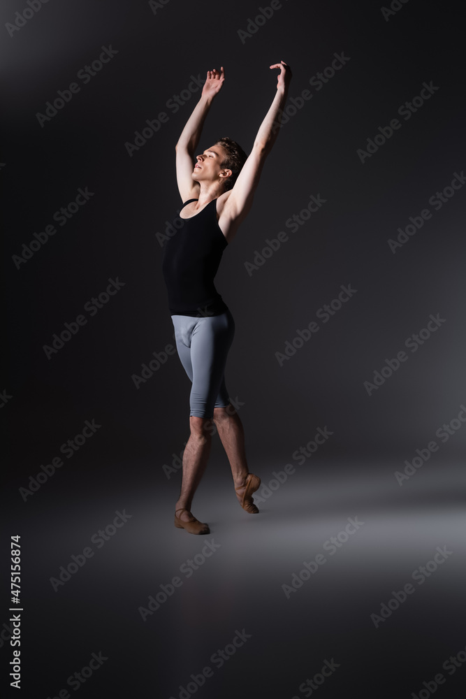 young and graceful man with outstretched hands performing ballet dance on black