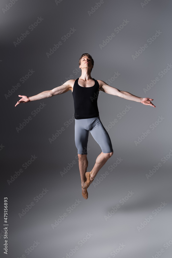 full length of elegant ballet dancer performing levitating with outstretched hands on dark grey