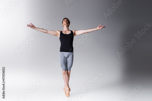 full length of young ballet dancer performing dance with outstretched hands on dark grey