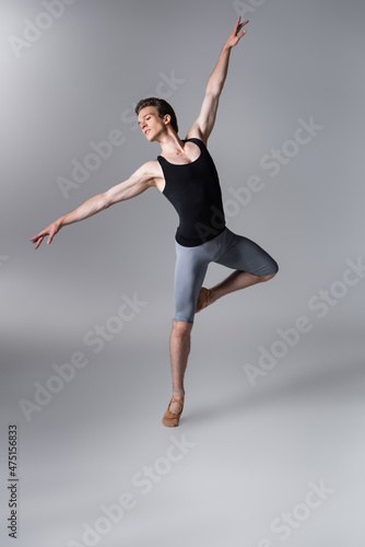 graceful young dancer gesturing while performing ballet dance on dark gray