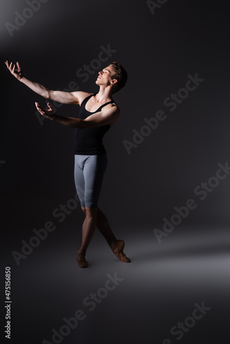 graceful dancer with outstretched hands performing ballet dance on black