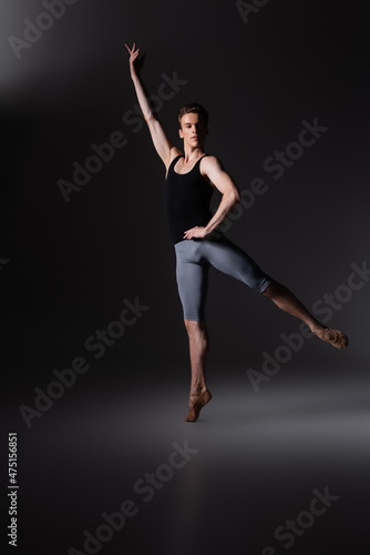 graceful man with outstretched hand performing ballet dance on black