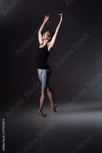 young and graceful man with outstretched hands performing ballet dance on black