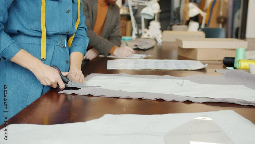Close-up of dressmakers' hands cutting material with scissors designing clothes working together in studio. Modern sewing workshop and people concept. Close-up of dressmakers' hands cutting material with scissors designing clothes working together in studio. Modern sewing workshop and people concept.