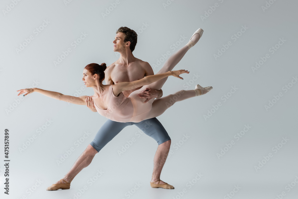 shirtless ballet dancer lifting young ballerina isolated on grey