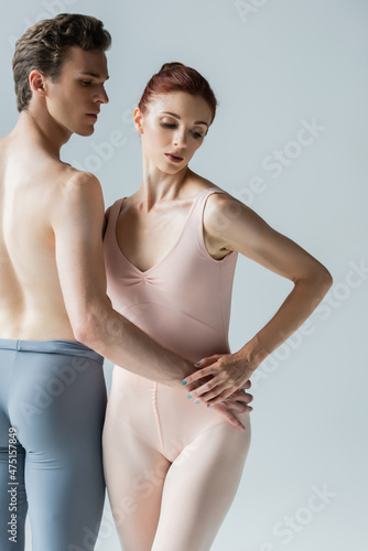 shirtless ballet dancer holding hand on hip of young ballerina isolated on grey