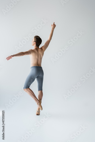 young shirtless ballet dancer with raised hand on grey