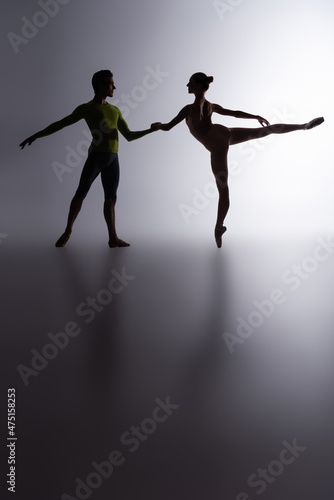 side view of graceful ballerina in bodysuit dancing with partner on dark grey © LIGHTFIELD STUDIOS