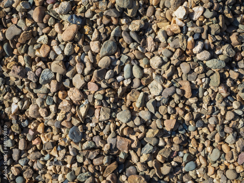 Small multicolored pebbles illuminated by the sun, close-up, natural textured background. Pebbles of different sizes and shapes top view Small multicolored pebbles illuminated by the sun, close-up, natural textured background. Pebbles of different sizes and shapes top view