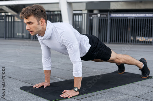 Young sportsman training outdoors, standing in plank pose