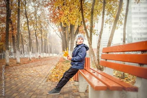 A boy in a blue jacket walks in an autumn park