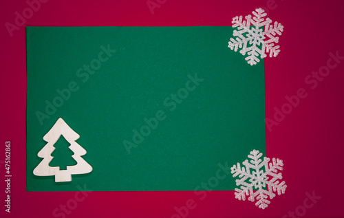 Minimalistyczne tło na kartkę z życzeniami świątecznymi w czerwonym i zielonym kolorze z białą choinką i płatkami śniegu.