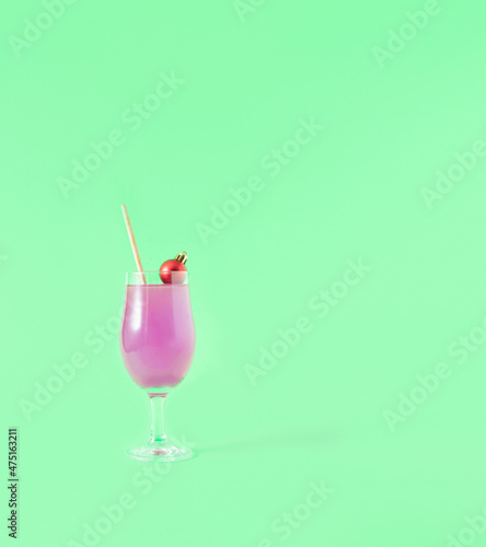 A cocktail decorated with a red Christmas ball on a green background. Minimal creative idea. Party concept.