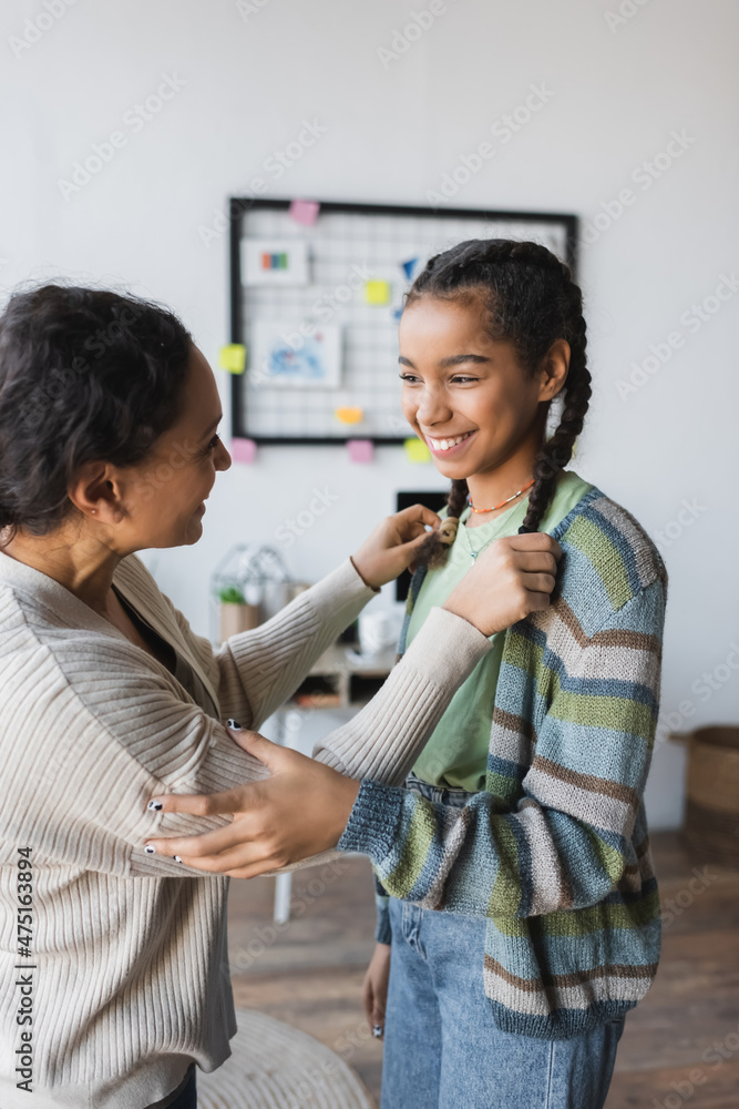 african american woman touching pigtails of happy teenage daughter african american woman touching pigtails of happy teenage daughter