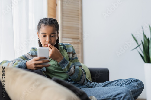 Obraz na plátně pensive african american girl looking at mobile phone on sofa at home