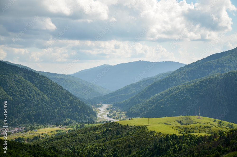 Rural landscape with green mountains covered with forest, grassy meadows, river and village. Carpathian, Ukraine.
