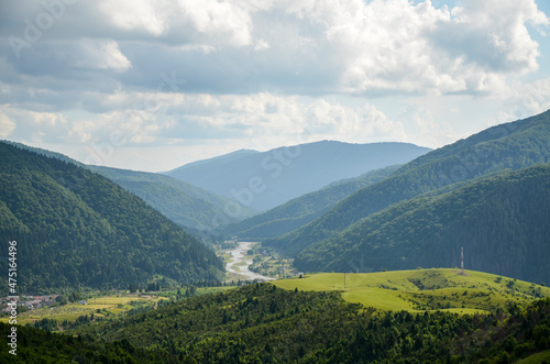 Rural landscape with green mountains covered with forest  grassy meadows  river and village. Carpathian  Ukraine.