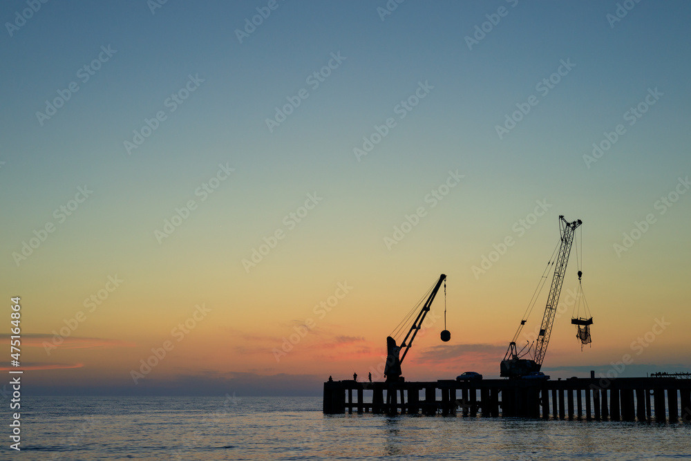 silhouettes of cranes at the shipyard, beautiful sunset at sea. empty pier silhouettes of cranes at the shipyard, beautiful sunset at sea. empty pier