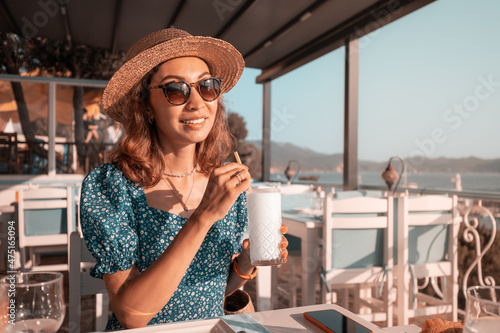 Girl traveler in hat drinks white cocktail or ayran in a rooftop bar overlooking the sea bay. photo