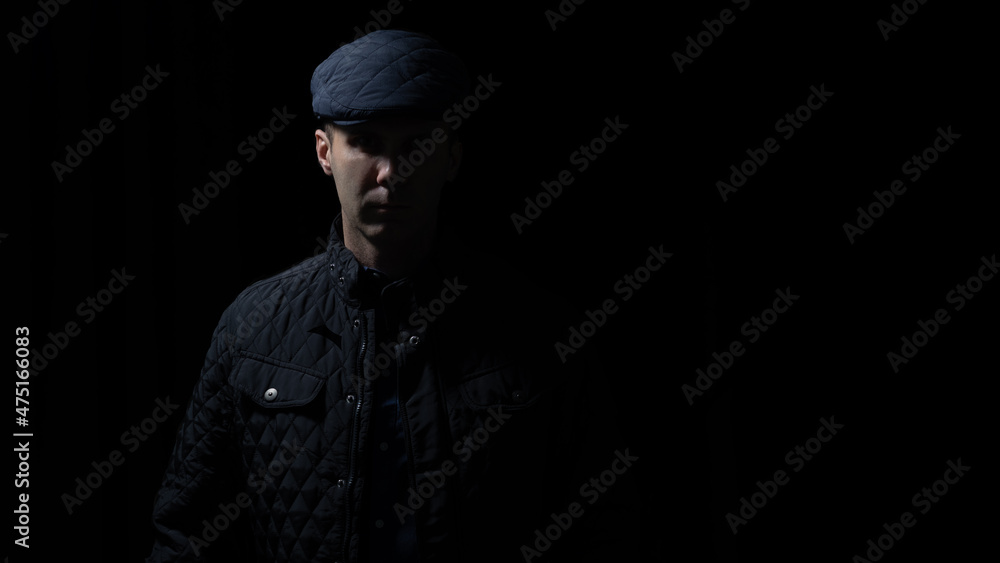 man in kepi and black jacket is staying in darkness, light and shadows on his face 