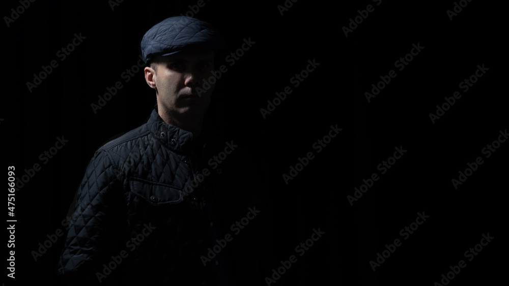 man in kepi and black jacket is staying in darkness, light and shadows on his face 