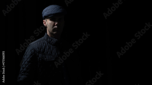 man in kepi and black jacket is staying in darkness, light and shadows on his face 