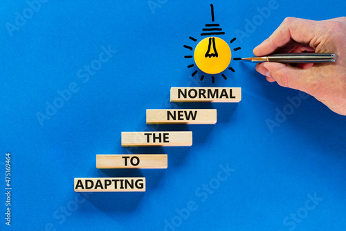 Adapting to the new normal symbol. Wooden blocks with words Adapting to the new normal on blue background, copy space. Light bulb icon. Businessman hand with pen. Business, new normal concept.