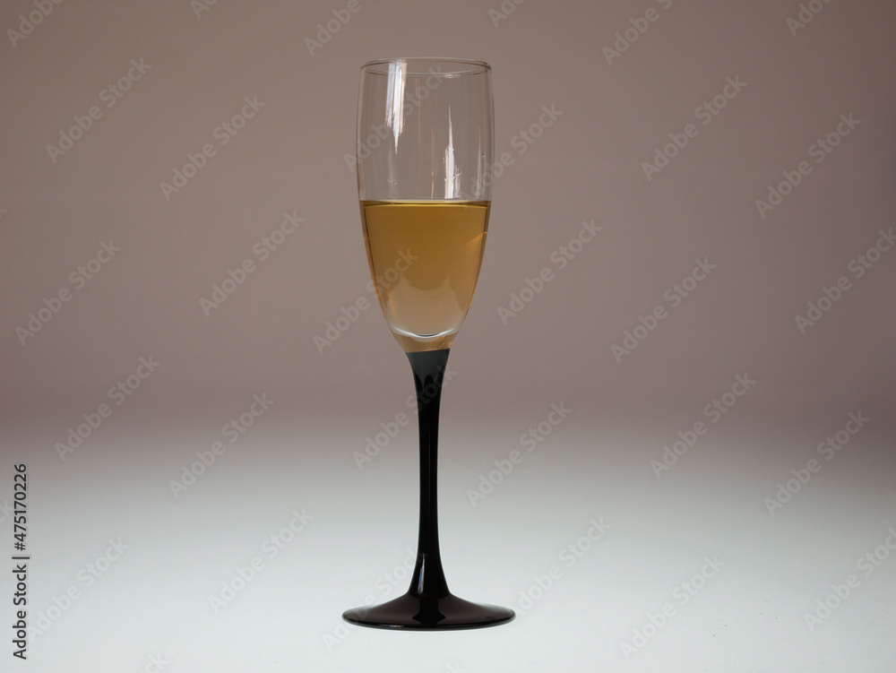 The glass filled with honey-colored wine on an illuminated light beige background The glass filled with honey-colored wine on an illuminated light beige background