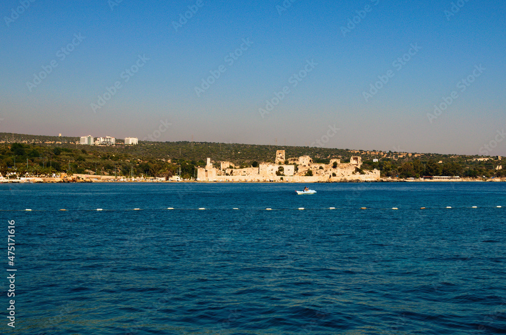Wide angle landscape view of blue water of Mediterranean Sea and city beach with ancient ruins of Romanian castle. Blue sky background. Famous touristic place