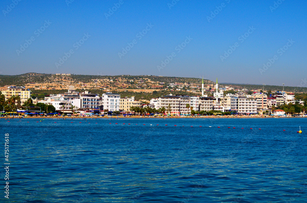 Kizkalesi, Turkey-11 October, 2021:Wide angle landscape view of blue water of Mediterranean Sea and city beach, embankment with many hotels in Kizkalesi. Blue sky background. Famous touristic place