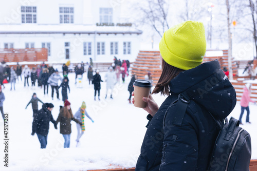 A girl drinks coffee from a paper cup on an open skating rink in Sevkabel in winter. Saint Petersburg, Russia