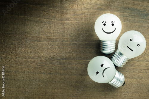 Satisfaction light bulb on wood background, excellent or happy smile face icon is glowing, with average and bad emotion as feedback and evaluation concept