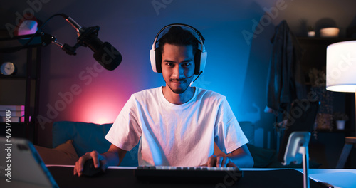 Young confident Asian man playing online computer video game, colorful lighting broadcast streaming live at home. Gamer lifestyle, E-Sport online gaming technology concept photo