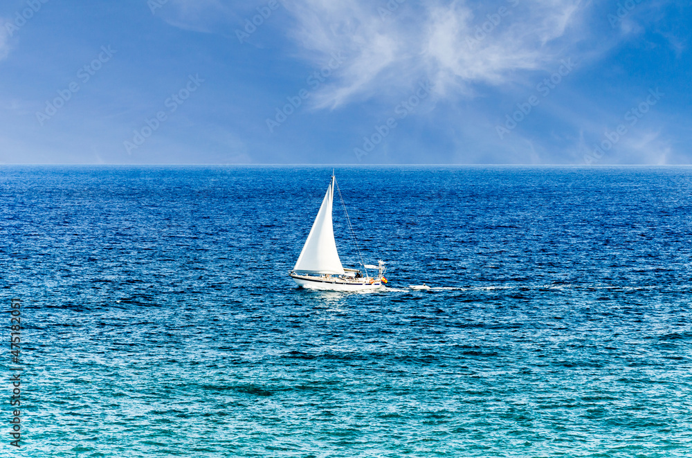 Fototapeta premium Scene of a small boat with sail in the middle of the blue ocean
