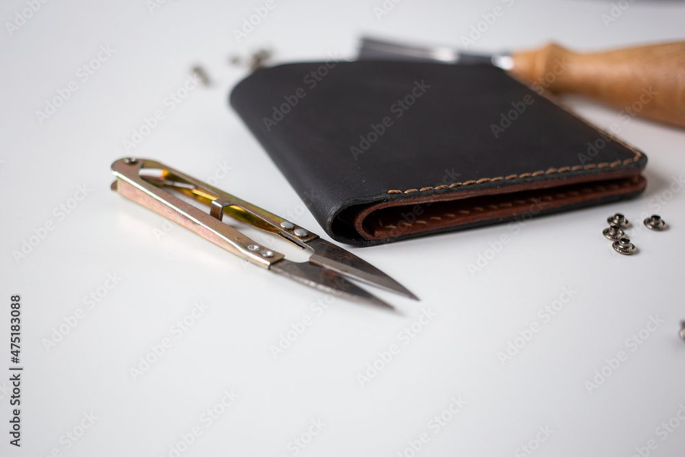 Leather wallet in black lies next to rivets and metal tools for leatherworking, leather product Leather wallet in black lies next to rivets and metal tools for leatherworking, leather product