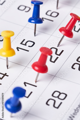 Colored push pins on monthly calendar page. Calendar appointments. Multicolored push pins on calendar. Marked event day, business appointment, meeting with pin. Close-up of push pins on calendar date